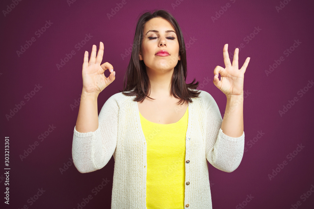 Young beautiful brunette woman a jacket over purple isolated background relax and smiling with eyes closed doing meditation gesture with fingers. Yoga concept. Young beautiful brunette woman a jacket over purple isolated background relax and smiling with eyes closed doing meditation gesture with fingers. Yoga concept.
