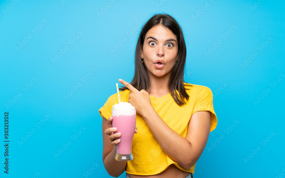 Young girl with strawberry milkshake over isolated background surprised and pointing side Young girl with strawberry milkshake over isolated background surprised and pointing side