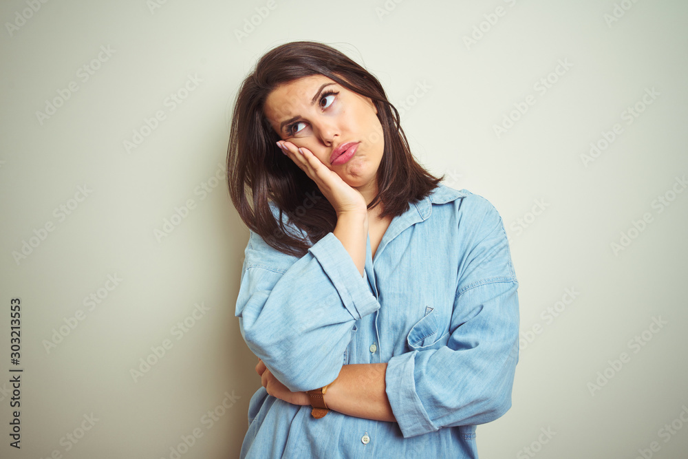 Young beautiful brunette woman wearing casual blue denim shirt over isolated background thinking looking tired and bored with depression problems with crossed arms. Young beautiful brunette woman wearing casual blue denim shirt over isolated background thinking looking tired and bored with depression problems with crossed arms.