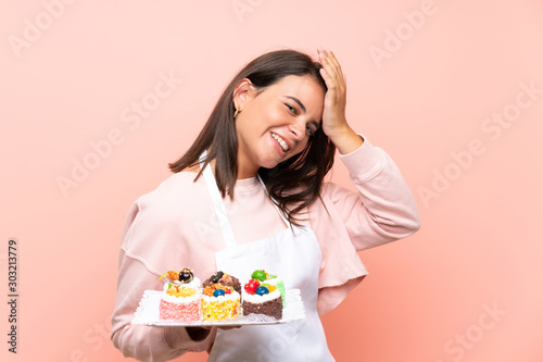 Young girl holding lots of different mini cakes over isolated background has realized something and intending the solution