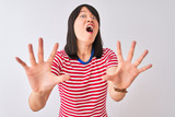 Young beautiful chinese woman wearing red striped t-shirt over isolated white background afraid and terrified with fear expression stop gesture with hands, shouting in shock. Panic concept.