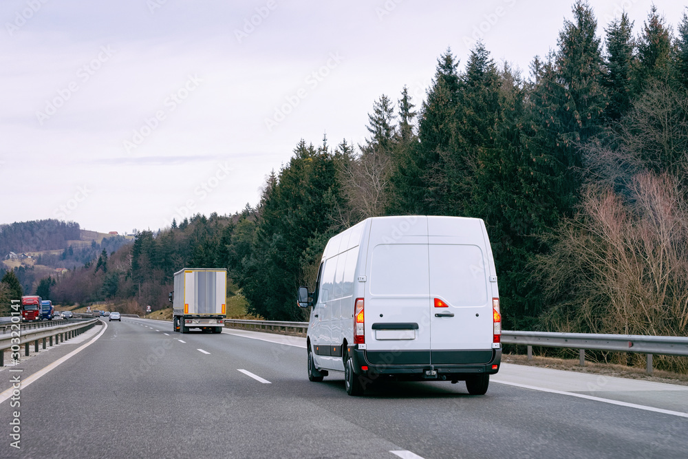 White Minivan in road. Mini van auto vehicle on driveway. European van transport logistics transportation. Auto with driver on highway.