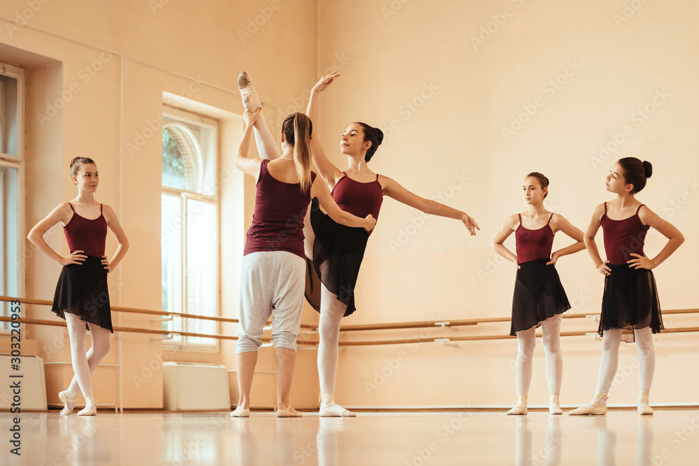 Ballet teacher assisting ballerina during exercise class at dance studio.