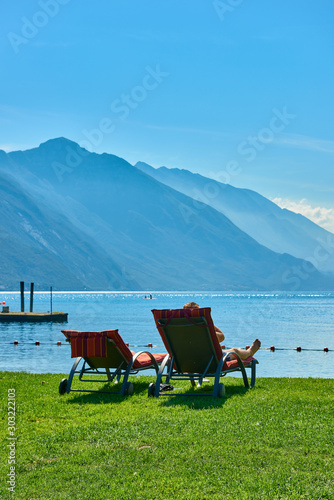 People sitting at the beach on the lounge chair and admiring Lake Garda in the summer time,View of the beautiful Lake Garda surrounded by mountains