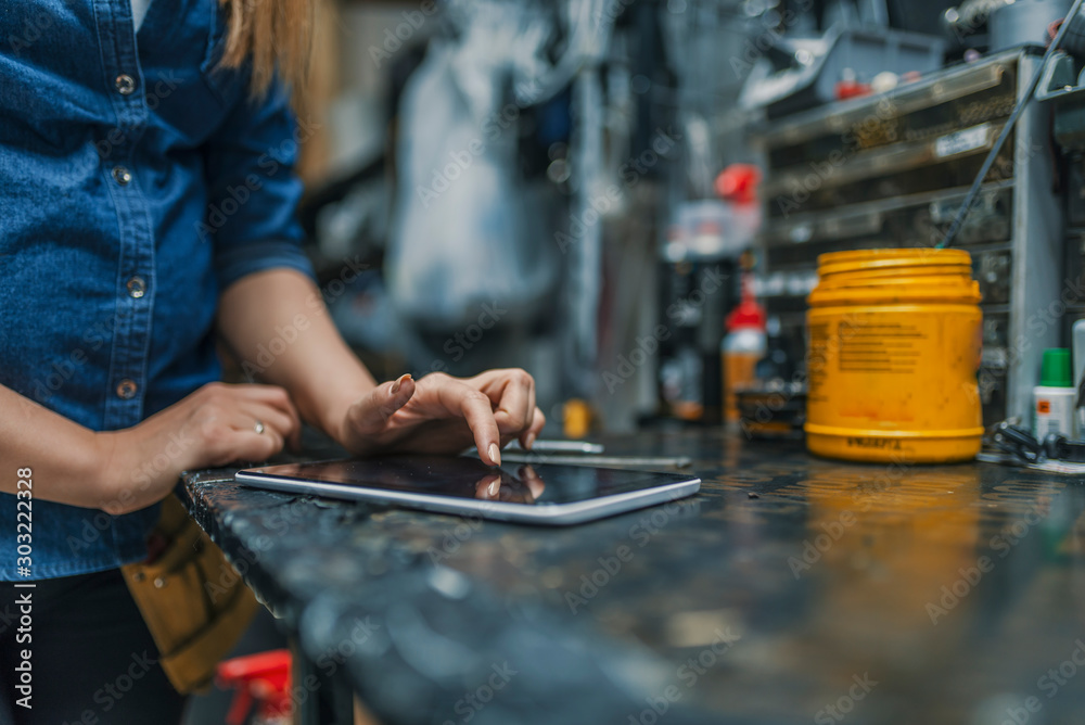 Female mechanic at work. Using a tablet while fixing a bicycle. Female bicycle repair technician using digital tablet in bicycle shop. Mechanic woman checking something on a tablet-pc and checklist. Female mechanic at work. Using a tablet while fixing a bicycle. Female bicycle repair technician using digital tablet in bicycle shop. Mechanic woman checking something on a tablet-pc and checklist.