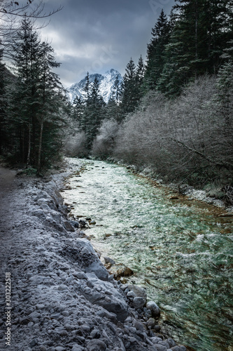 Cold green river stream in the Alps in winter. Mountain river water landscape with trees and blue sky in the background. River coast with rocks. 