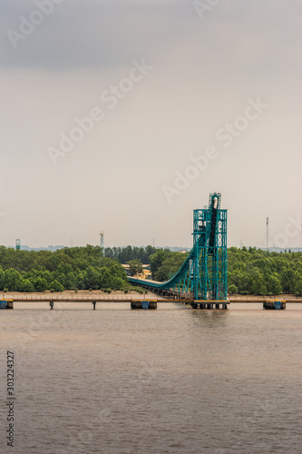 Long Tau River, Vietnam - March 12, 2019: Portrait, Azure blue dock and pipeline installation built on brown water to handle tankers at Phuoc Khanh Petroleum port. Green belt and foggy sky. photo