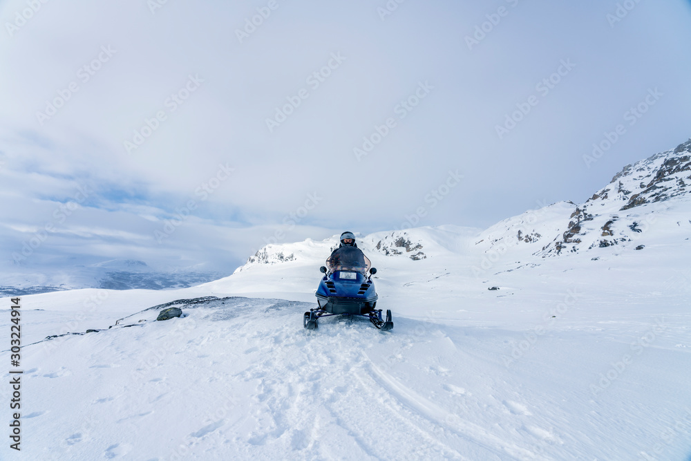 Young boy dressed for winter cold weather drives blue snowmobile in Swedish mountains. Joesjo, Lappland Northern Sweden