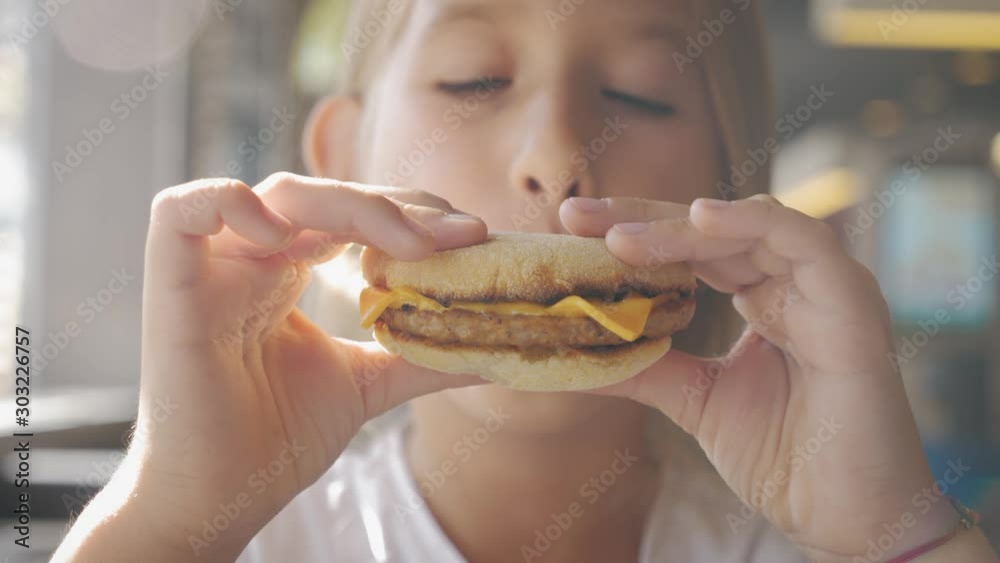 Beautiful happy hungry baby girl eating hamburger. Fast food concept. Tasty unhealthy burger sandwich in hands. Beautiful happy hungry baby girl eating hamburger. Fast food concept. Tasty unhealthy burger sandwich in hands.