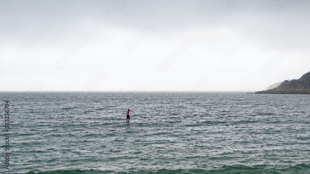 Rear view of young sportsman paddling on stand up paddleboard, sailing alone on sea.