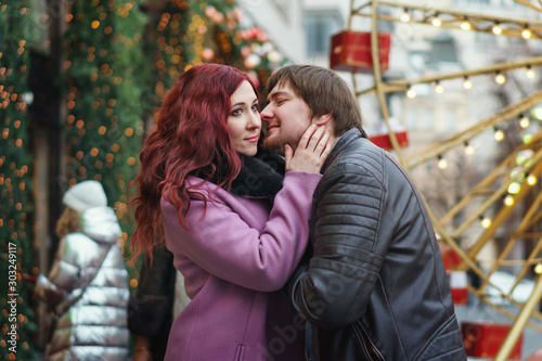 Loving couple in festive Christmas city celebrate the New Year. Romantic walk in winter. Having fun in winter christmas fair market decorations at central square city. Vacation and holiday concept