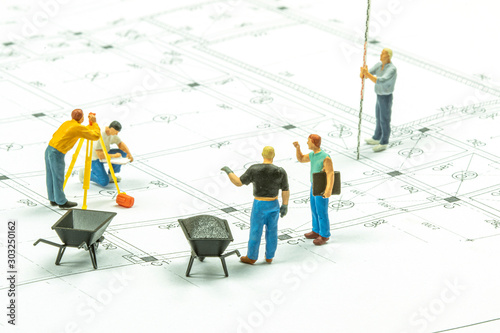 Miniature people surveyor technician is measuring the distance to build a house.