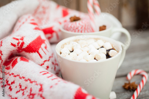 Coffee with marshmallows, knitted sweater with deer, candy cane on wooden background. Winter background