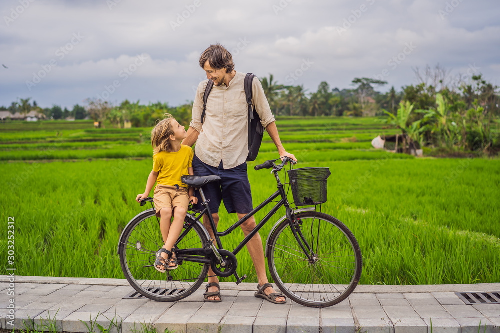 Father and son ride a bicycle on a rice field in Ubud, Bali. Travel to Bali with kids concept Father and son ride a bicycle on a rice field in Ubud, Bali. Travel to Bali with kids concept