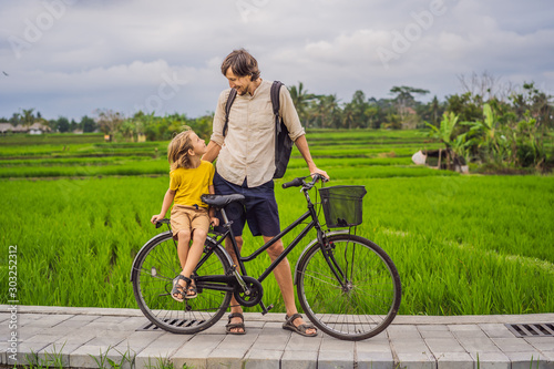 Father and son ride a bicycle on a rice field in Ubud, Bali. Travel to Bali with kids concept