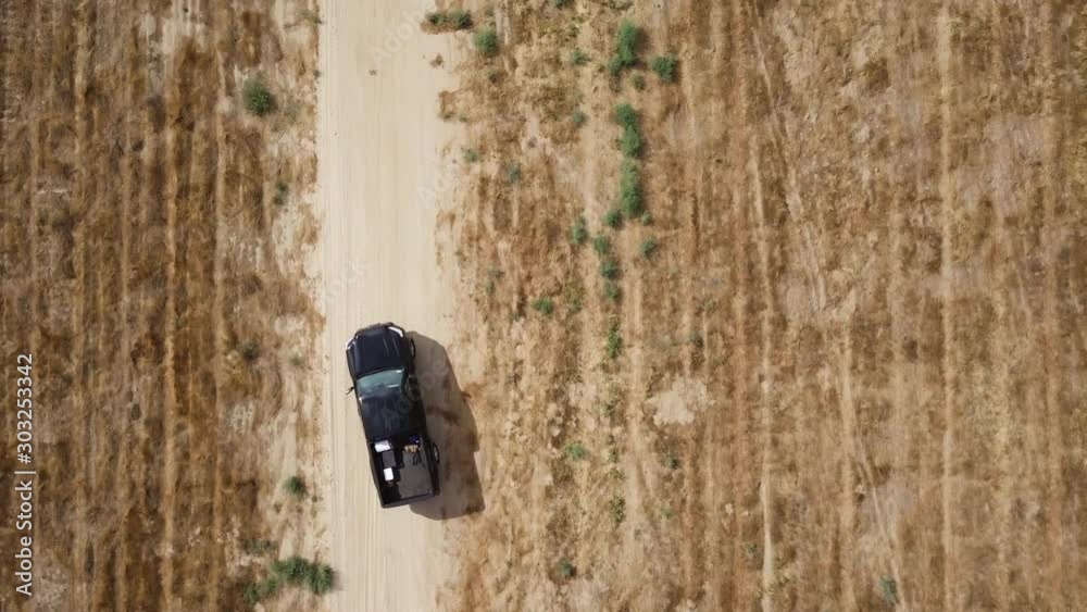 Black pick up is taking off the side of the road and drives along the deserted road. Aerial shot, top view Black pick up is taking off the side of the road and drives along the deserted road. Aerial shot, top view