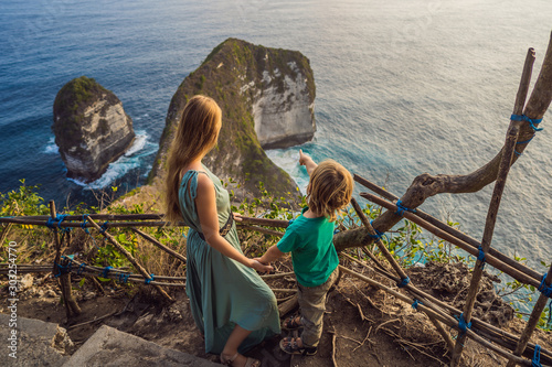 Family vacation lifestyle. Happy mother and son stand at viewpoint. Look at beautiful beach under high cliff. Travel destination in Bali. Popular place to visit on Nusa Penida island