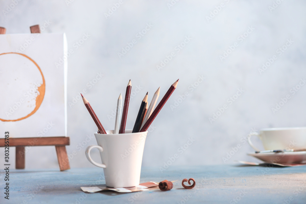 Coffee cup with pencils in front and of coffee stain painting on an easel. Creative workplace Coffee cup with pencils in front and of coffee stain painting on an easel. Creative workplace