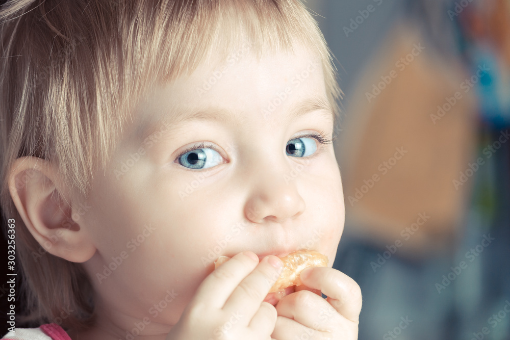 Beautiful child with big blue eyes eating orange slice Beautiful child with big blue eyes eating orange slice