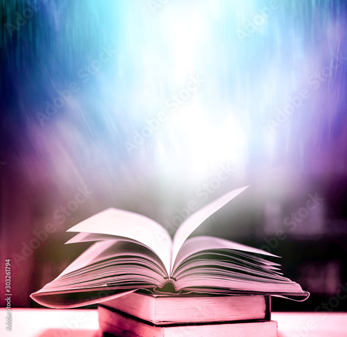 Open an old book with magical light magic on an ancient table in a dark room. © Ping198