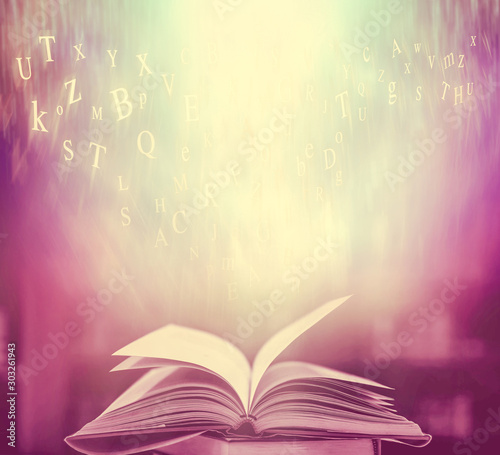  Imagine opening an old book blurred with magic power on the table and the English alphabet floating above the book with magic light as a beautiful background design. © Ping198