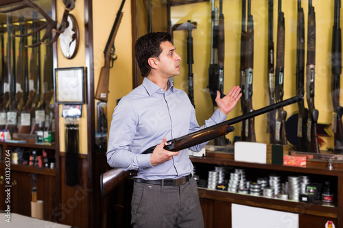 Man owner of hunting shop offering shotgun indoors