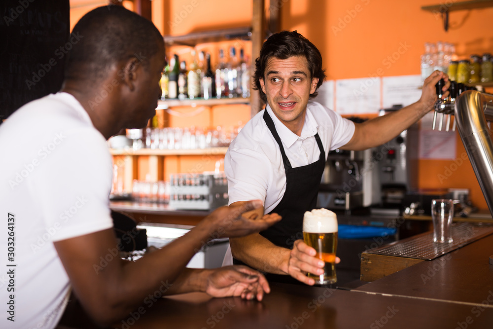 Smiling man barman giving glass of golden beer to client