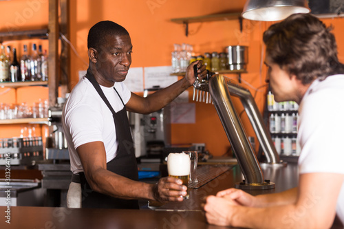 Young man bartender giving beer with foam to man client