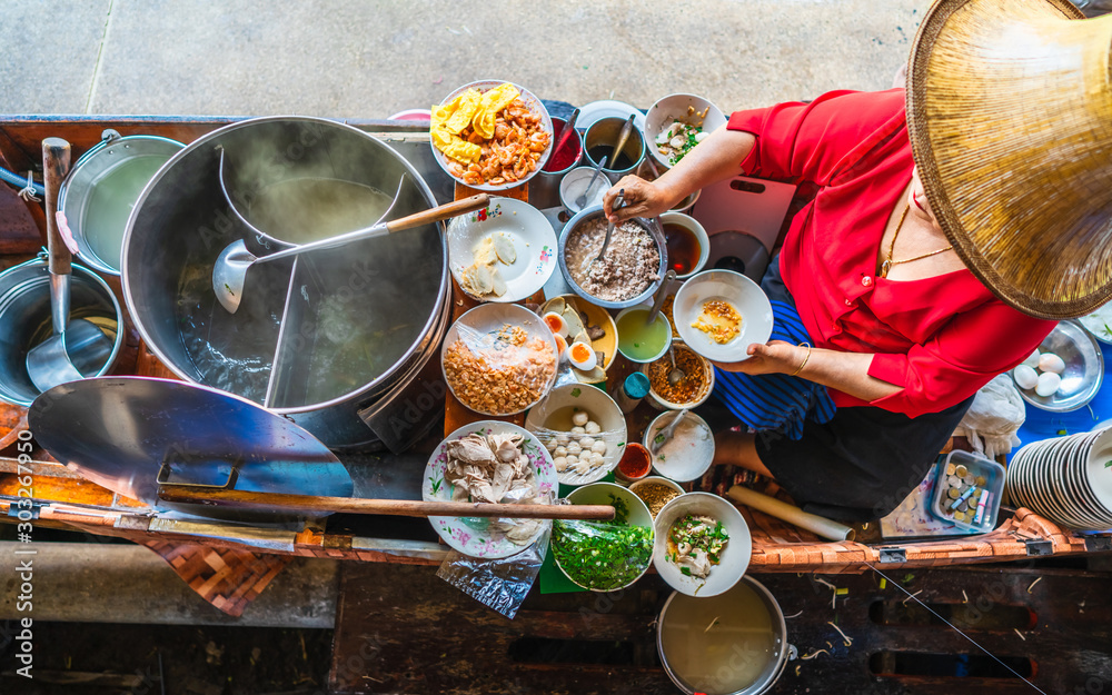 Fototapeta premium Widok z góry stara kobieta gotująca tajską zupę z makaronem w stylu Tom Yam na tajskiej tradycyjnej łodzi na lokalnym pływającym targu, słynne tradycyjne tajskie jedzenie uliczne dla turystów podróżujących po Bangkoku w Tajlandii, smaczna Azja