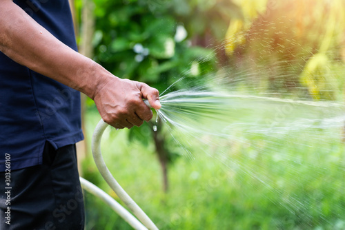 Watering plants in the garden, irrigating the soil. Garden work. The man is watering plants in the garden. A view of a man holding a coat. Saving water, care of plants. 