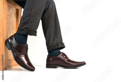 Elegant man in business dress wearing brown shoes sitting on wood box and resting his leg on floor white background.