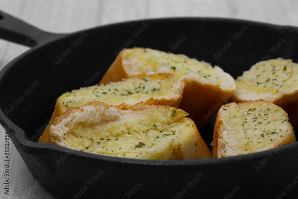 Garlic bread with herbs in a cast iron frying pan.  On a grey wood background