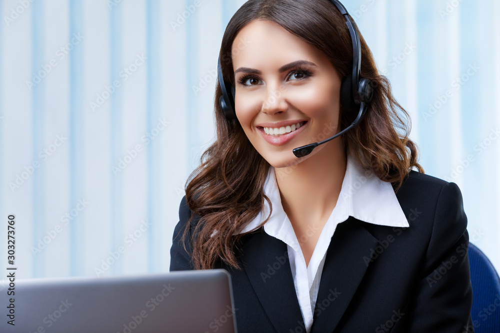 Portrait of young customer support female phone operator or sales agent in headset and confident black suit, working with laptop at office workplace. Consulting and assistance service call center. Portrait of young customer support female phone operator or sales agent in headset and confident black suit, working with laptop at office workplace. Consulting and assistance service call center.