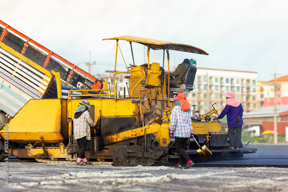 Many workers with equipment helped to build or paver the road with asphalt compactor finisher machine in the afternoon