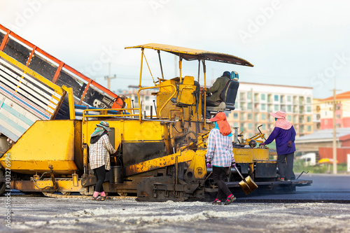Many workers with equipment helped to build or paver the road with asphalt compactor finisher machine in the afternoon