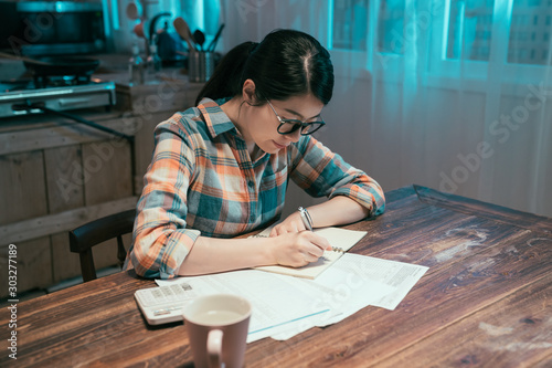 attractive young asian korean housewife wears glasses at home stay up late in night. girl examines gas and electricity bills. female considers spending this month and under stress checking accounts