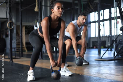 Obraz Fit and muscular couple focused on lifting a dumbbell during an exercise class in a gym.