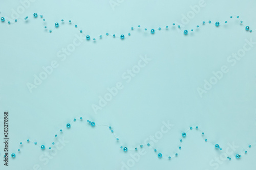 Christmas frame. Christmas shiny, glossy beads decorations on turquoise background. Concept for celebration, carnival, party, festive sales. Flat lay, top view, copy space.