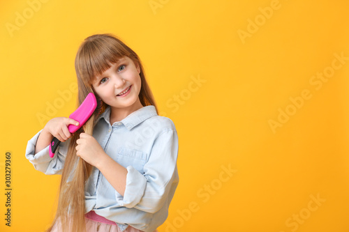 Cute little girl brushing hair on color background