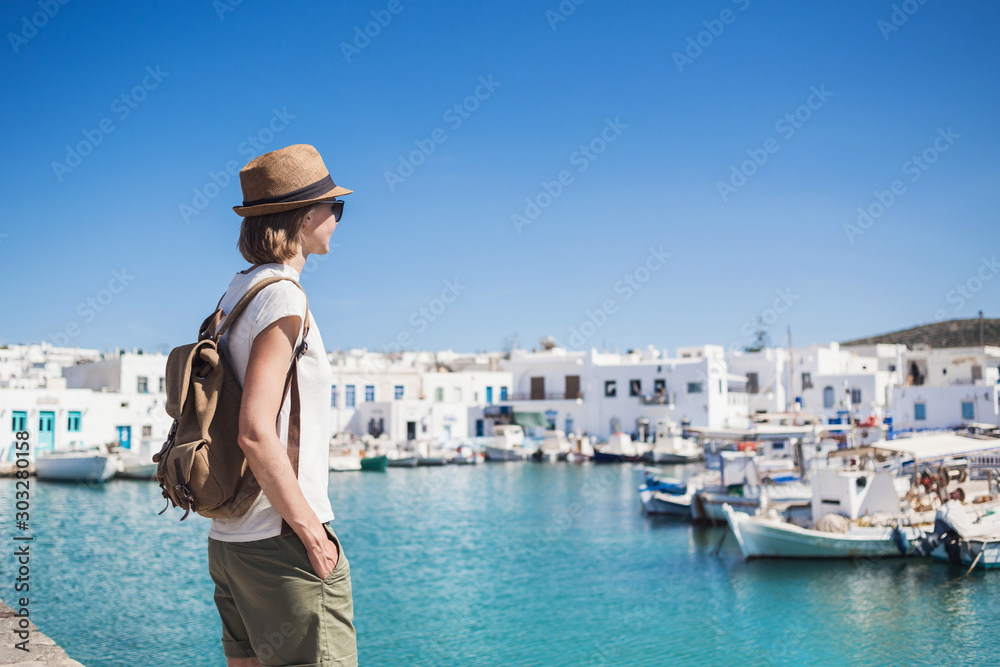 Young woman wearing hat looking at greek village with sea. Traveler girl enjoying vacation in Greece. Summer holidays, vacations, travel, tourism concept.