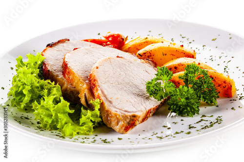 Roasted pork with baked potatoes and vegetables on white plate