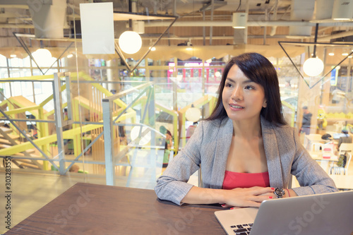 Social media Asian woman siting with laptop in the room looking out to camera, workplace background