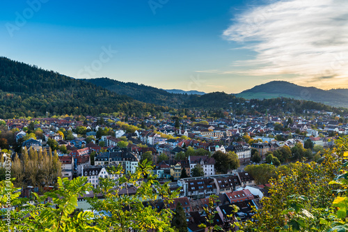 Germany, Aerial view above freiburg im breisgau city skyline with houses, church and streets surrounded by black forest nature landscape in warm orange sunset light