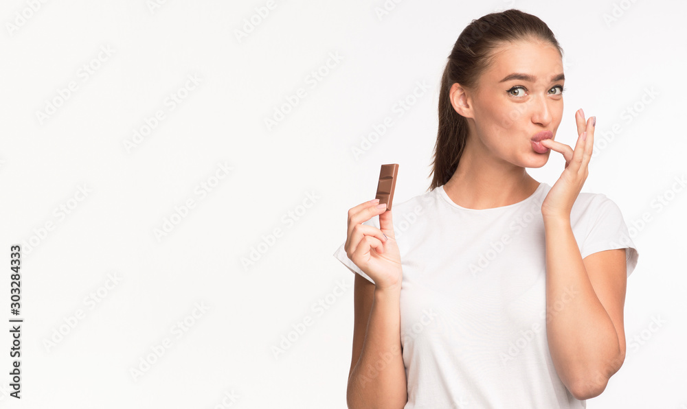 Girl Eating Chocolate And Licking Finger Standing On White Background Girl Eating Chocolate And Licking Finger Standing On White Background