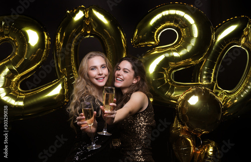 Two young ladies drinking champagne. Image of girls with balloons isolated on black background.