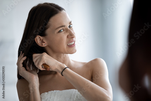 фотографія Stressed young lady brushing long tangled hair looking in mirror