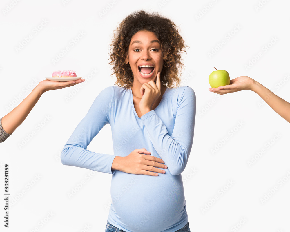 Pregnancy nutrition. Emotional pregnant woman choosing between apple and donut Pregnancy nutrition. Emotional pregnant woman choosing between apple and donut