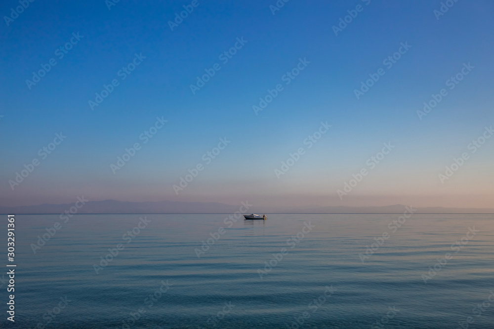 Beautiful early morning peaceful sea landscape. Small boat, blue calm sea water and clear sky. Horizontal color photography.