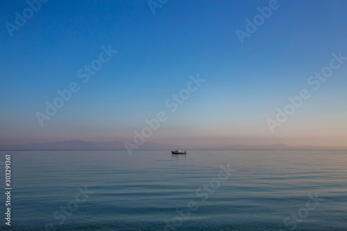 Beautiful early morning peaceful sea landscape. Small boat, blue calm sea water and clear sky. Horizontal color photography.