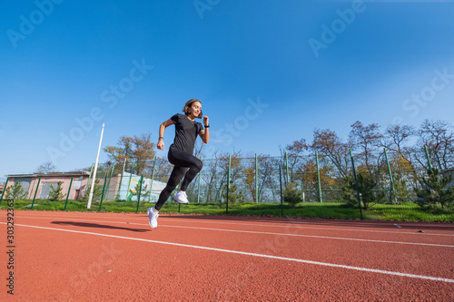Young female runner training in summer day outdoors on the studium © serejkakovalev
